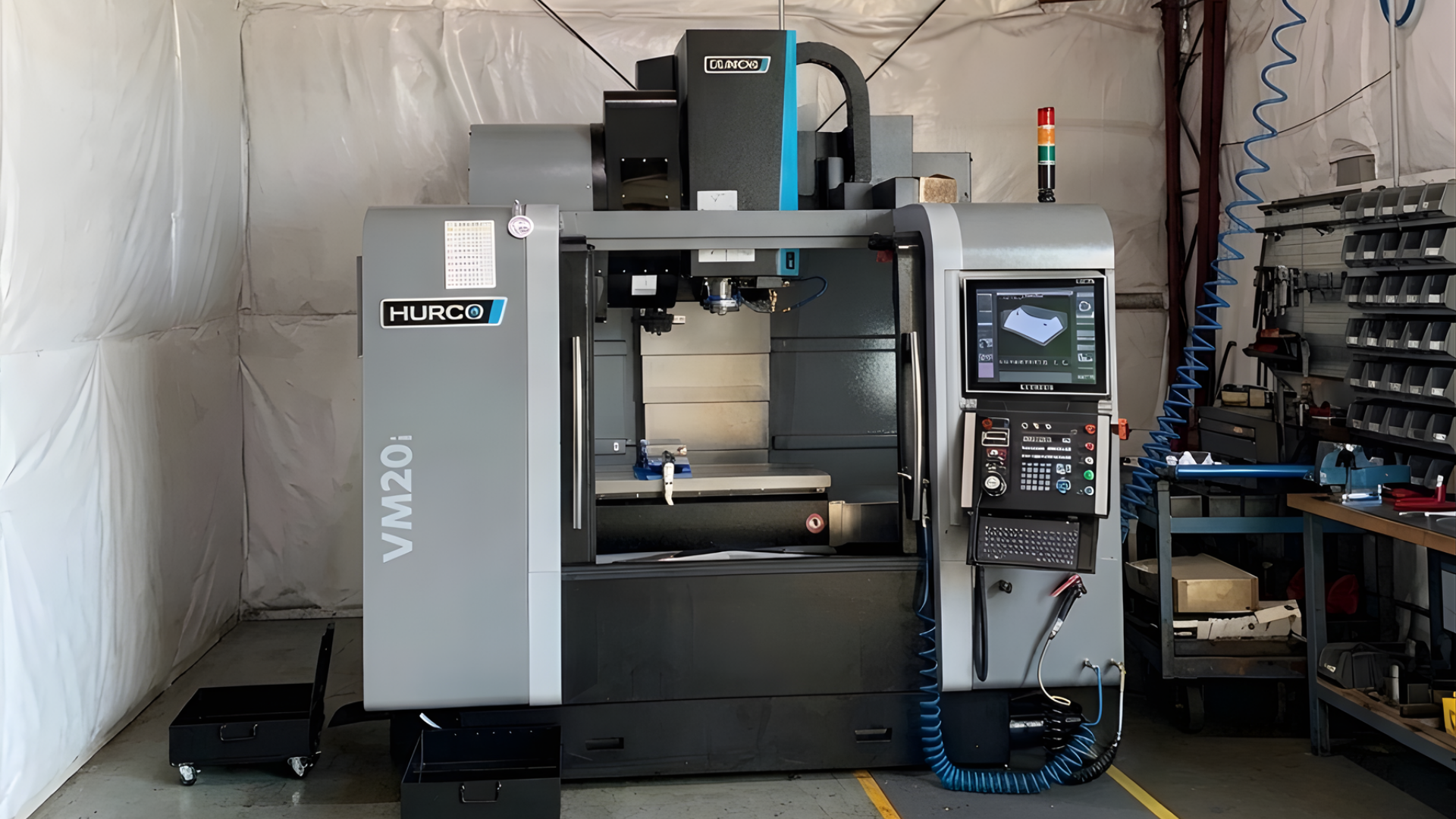 Large gray CNC machine in an industrial workshop with a control panel and stacked parts nearby