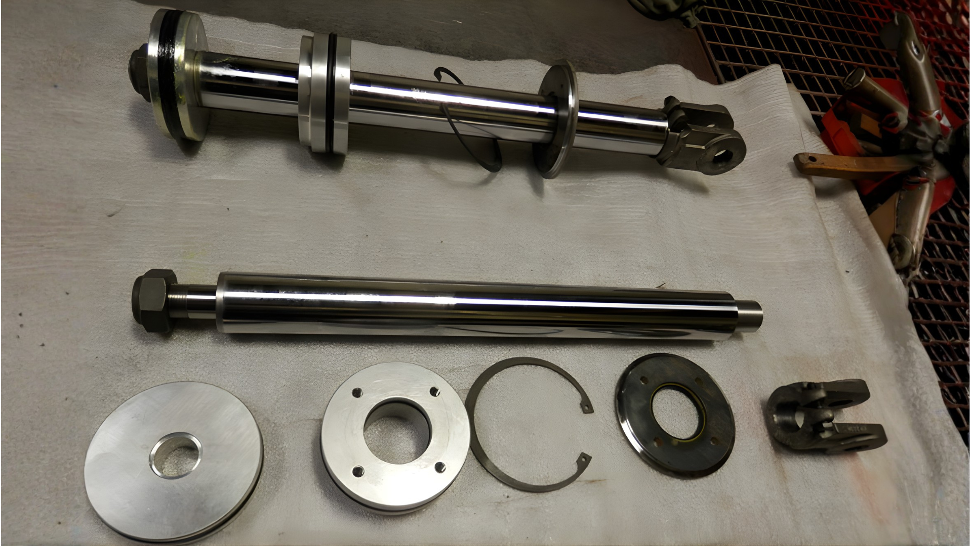 Disassembled metal shaft and parts laid out on a workbench, with bolts, discs, and clips.