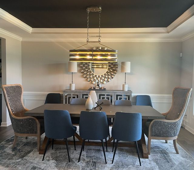Dining room with gray walls, dark ceiling, large table with blue chairs, and a decorative chandelier.