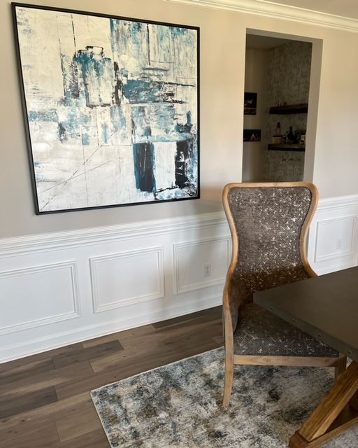 Abstract blue and white painting over a dining chair with a textured back in a dining room.