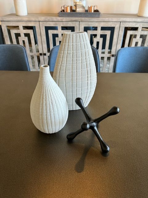Two textured vases and a black decorative jack on a brown table. Blue chairs and a wood cabinet in the background.