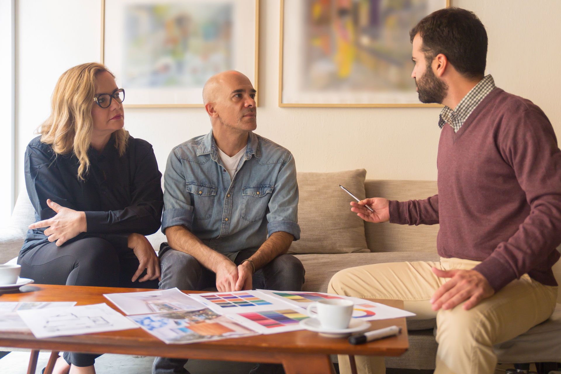 Three people talking in a living room, with papers spread across a coffee table.