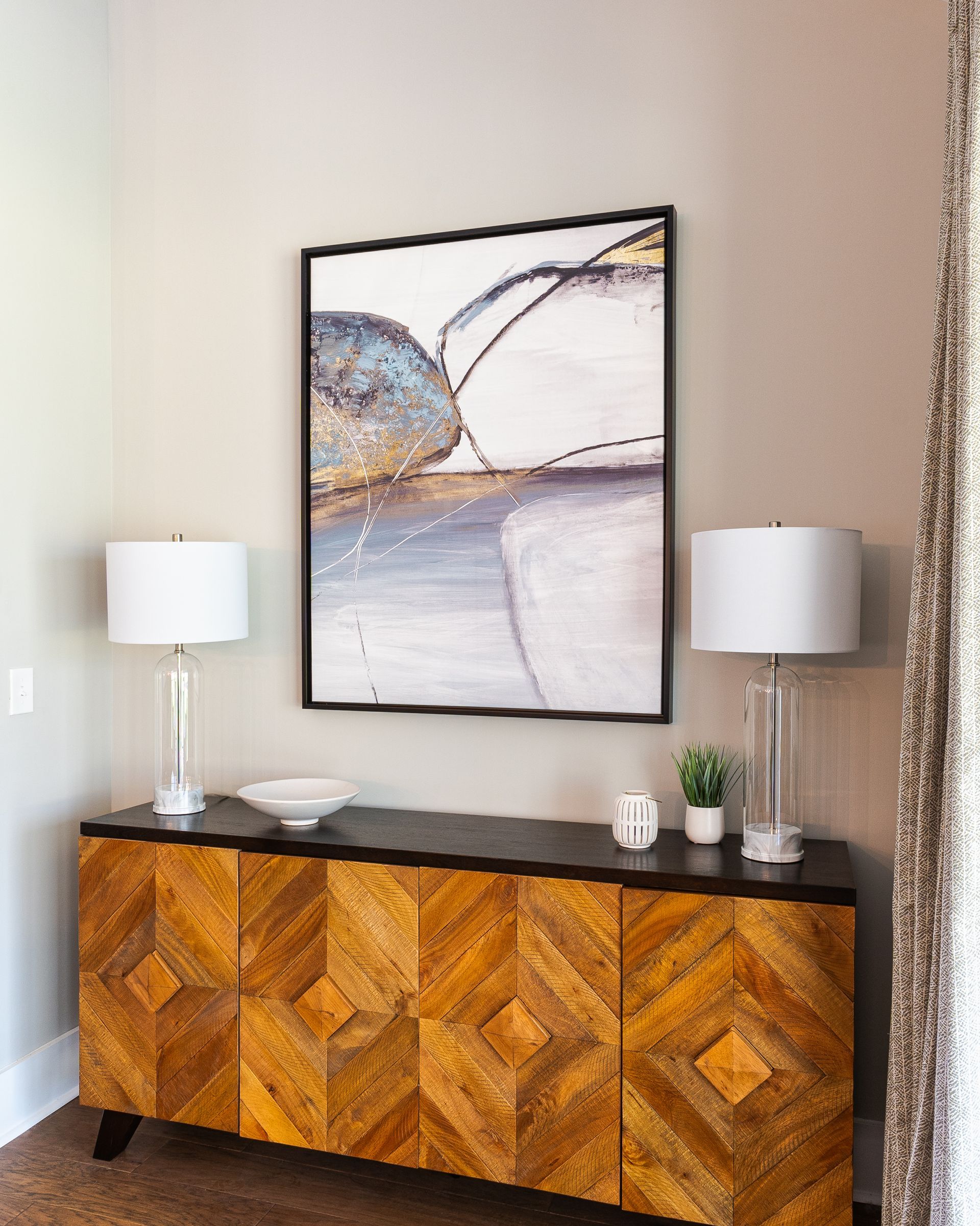 A wooden console table with lamps and art on a light beige wall.