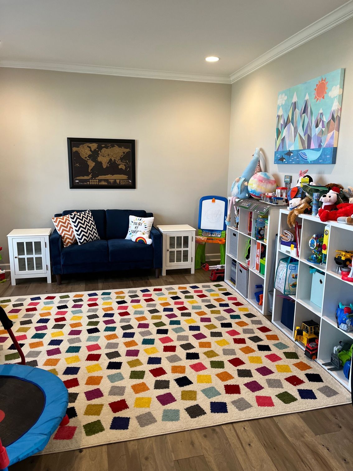 Playroom with blue sofa, colorful rug, toy shelves, and a small trampoline.