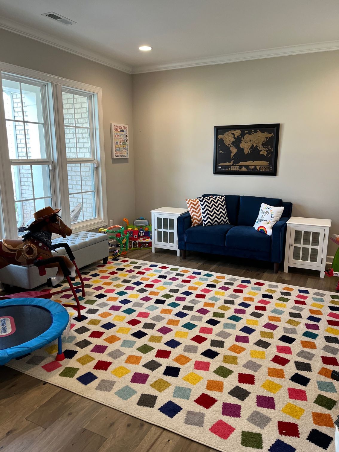 Playroom with a colorful rug, blue couch, toy horse, and windows.