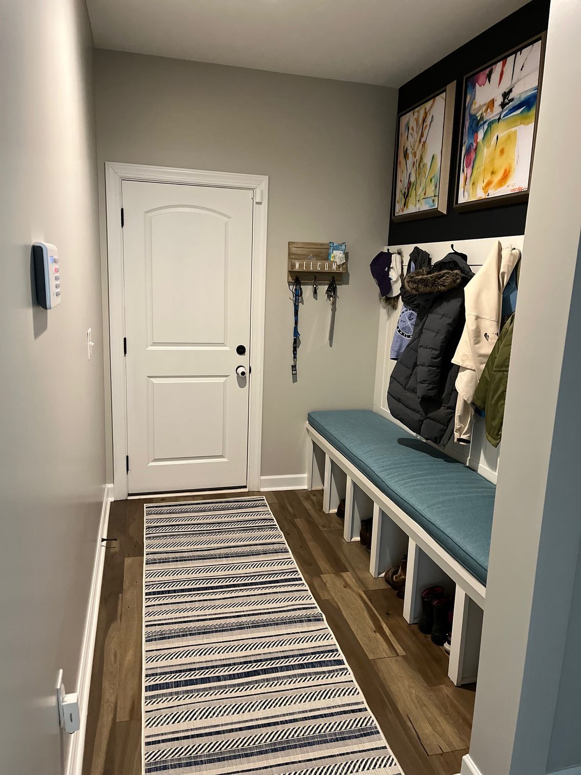 Entryway with coat rack, bench, and door. Blue, gray, and white decor. Artwork on the wall above.