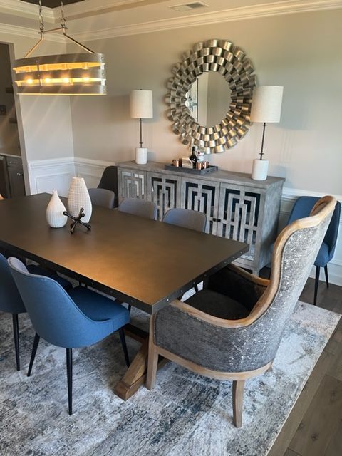 Dining room: dark table with blue chairs, gray sideboard, silver sunburst mirror, and a chandelier.
