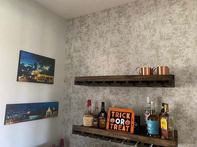 A home bar with wooden shelves, alcohol bottles, and Halloween decor against a textured wallpaper.