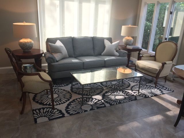 Living room with gray sofa, two cream chairs, patterned rug, two lamps, and coffee table.