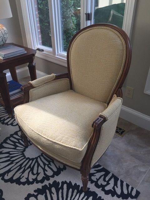 Cream upholstered armchair with dark wooden frame near a window and small table.