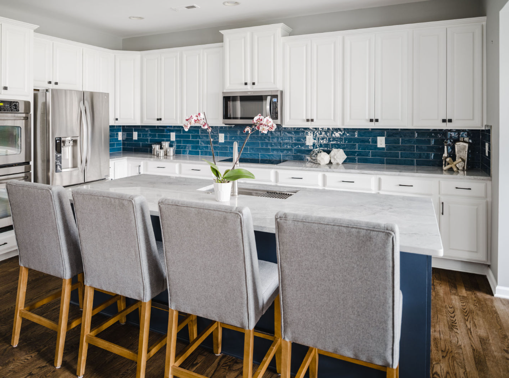 Modern kitchen with white cabinets, blue backsplash, gray island, and bar stools.