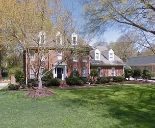 Two-story brick house with dormers and green lawn under a sunny sky.