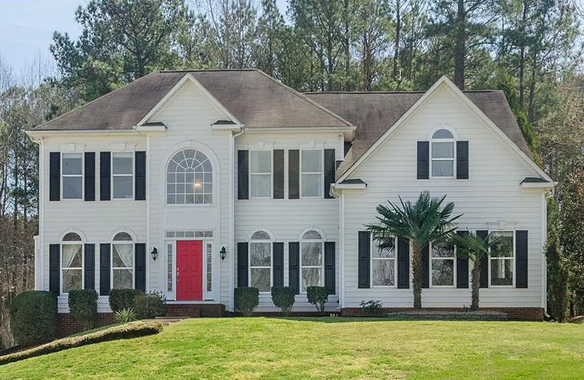 White two-story house with black shutters, red front door, and green lawn.