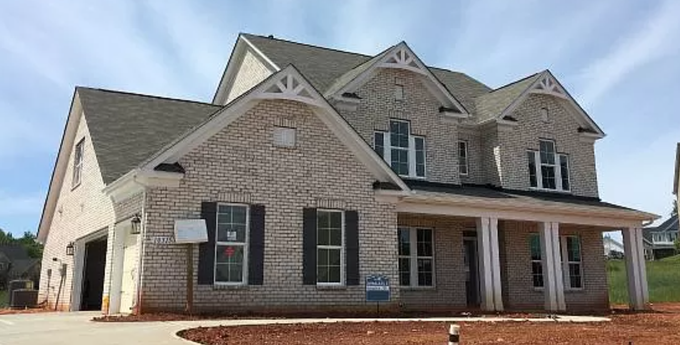 Two-story brick house with a porch, garage, and blue sky background.