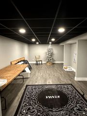 Modern room with a long wooden table, black rug, chair, and decorated Christmas tree under recessed lights
