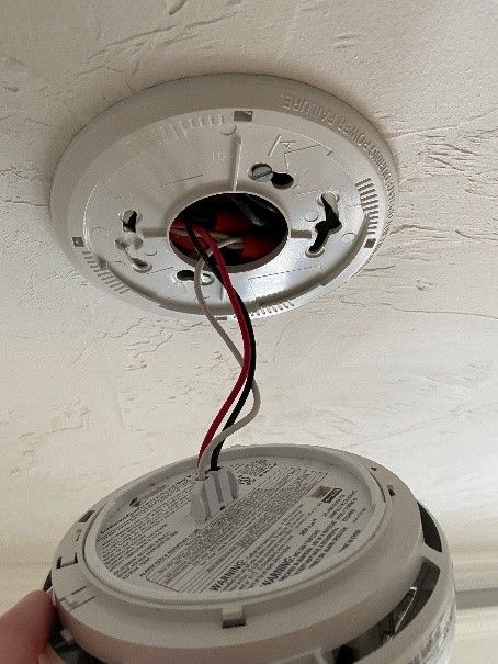 Detached ceiling smoke alarm with exposed red and black wires hanging down