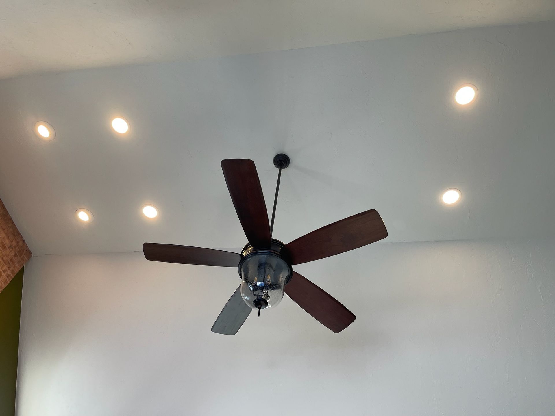 Ceiling with recessed lights and a dark-blade ceiling fan in a white room
