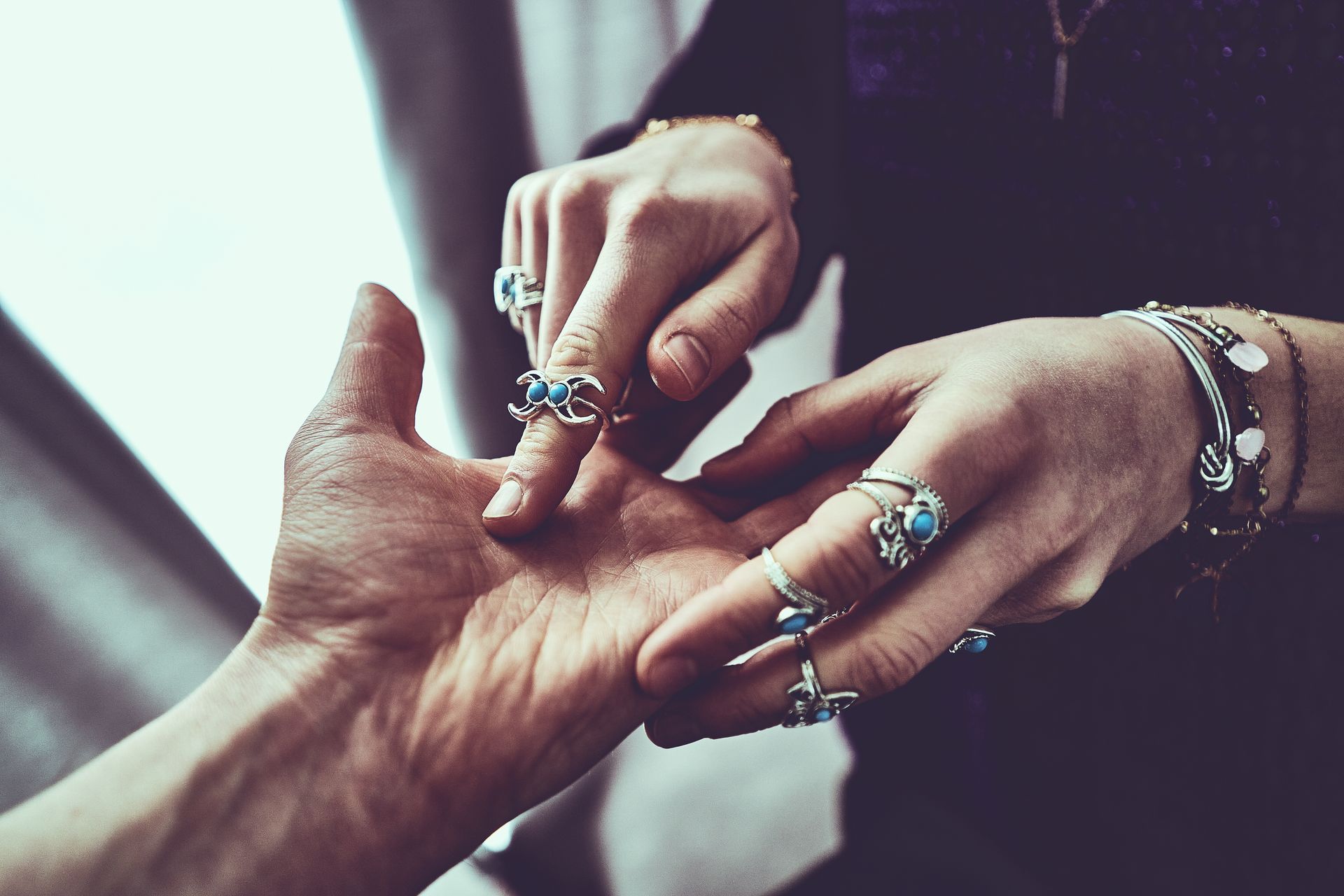 A person's palm is read by someone with many rings. Close-up, indoors.