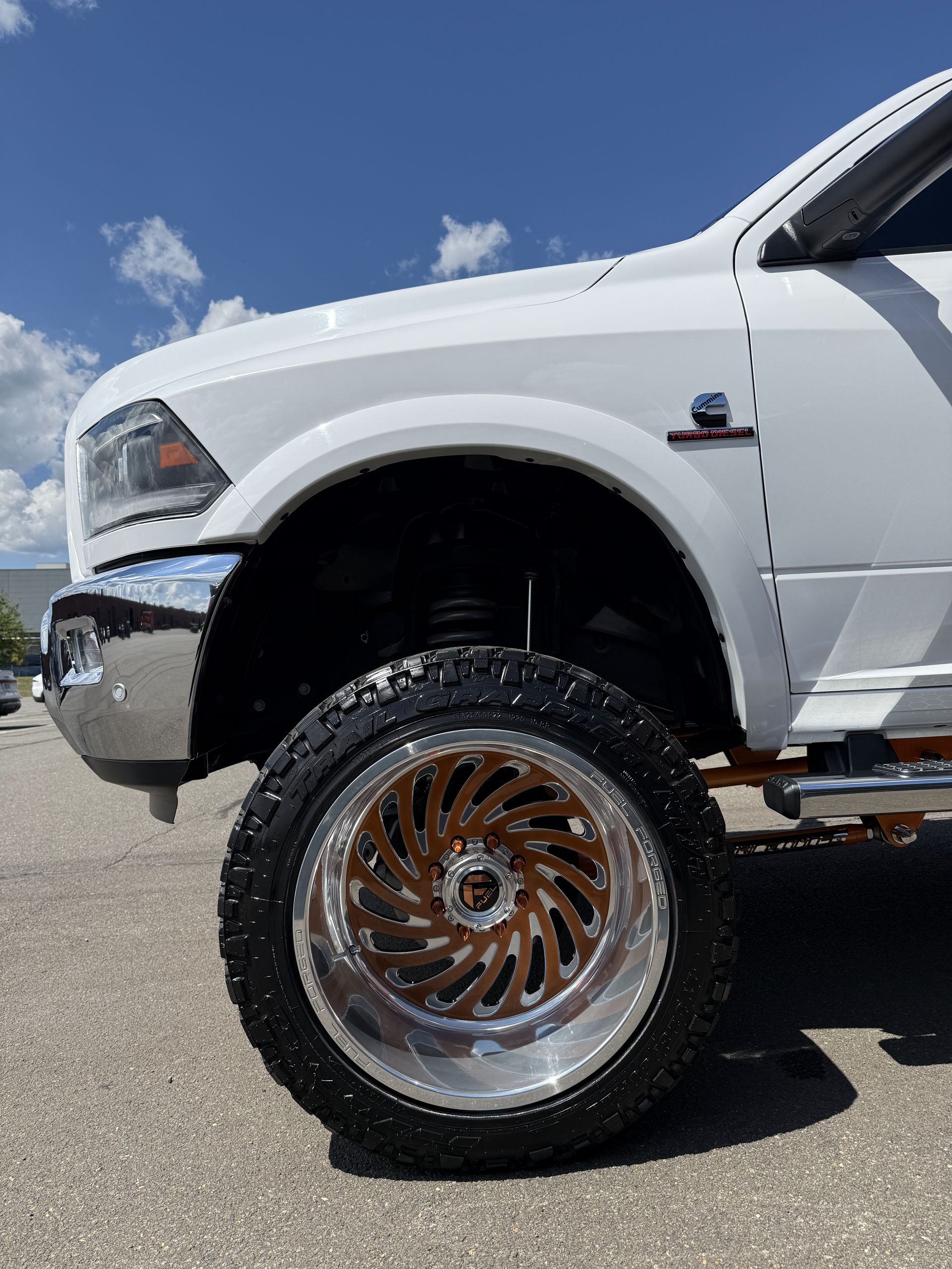 White lifted truck with chrome wheel and large off-road tire on pavement under a blue sky
