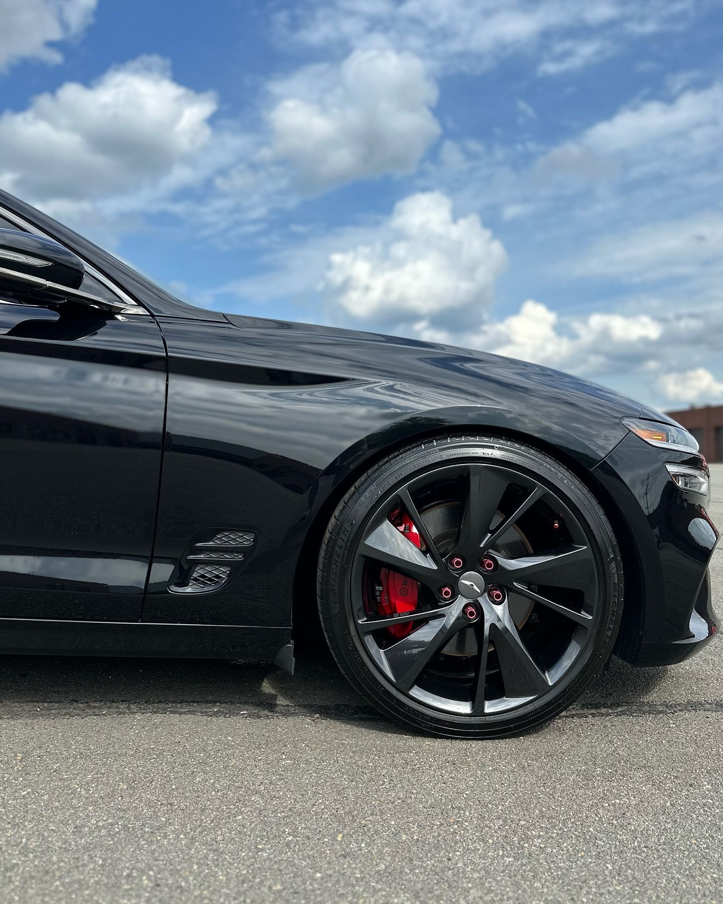 Black sports car with red brake calipers parked under a cloudy blue sky