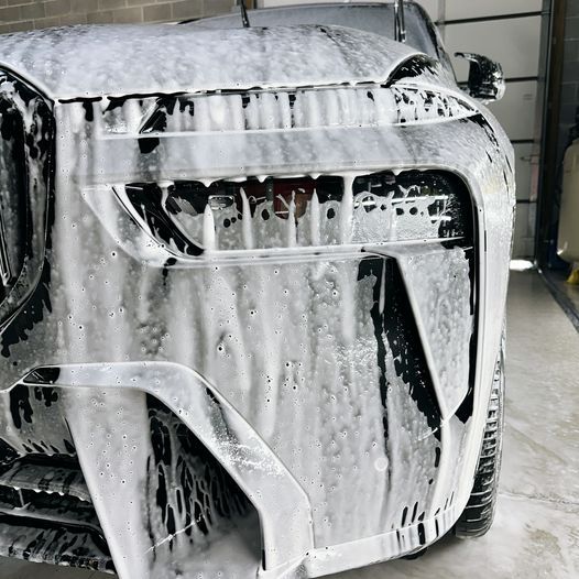 Car front covered in thick white soap foam during a car wash