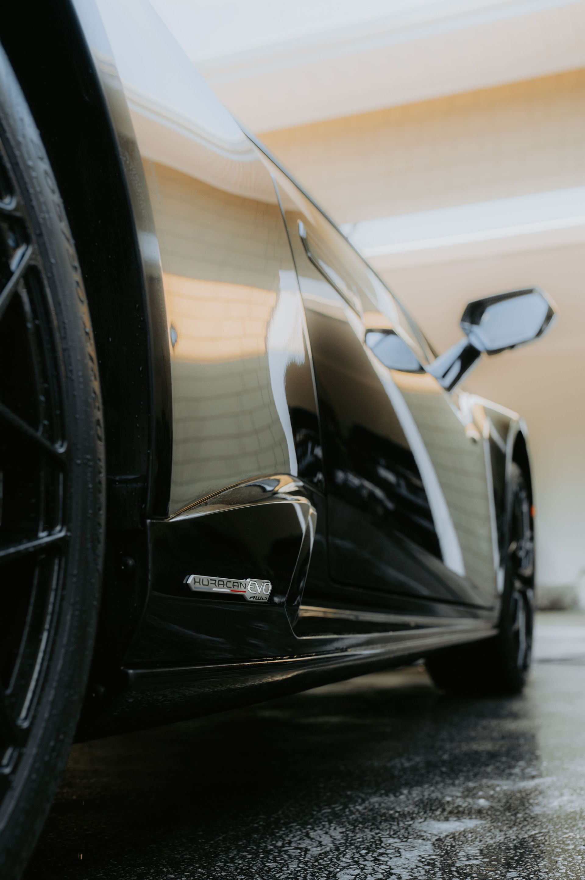 Low-angle view of a sleek black sports car in a wet garage, showing its side and front wheel.