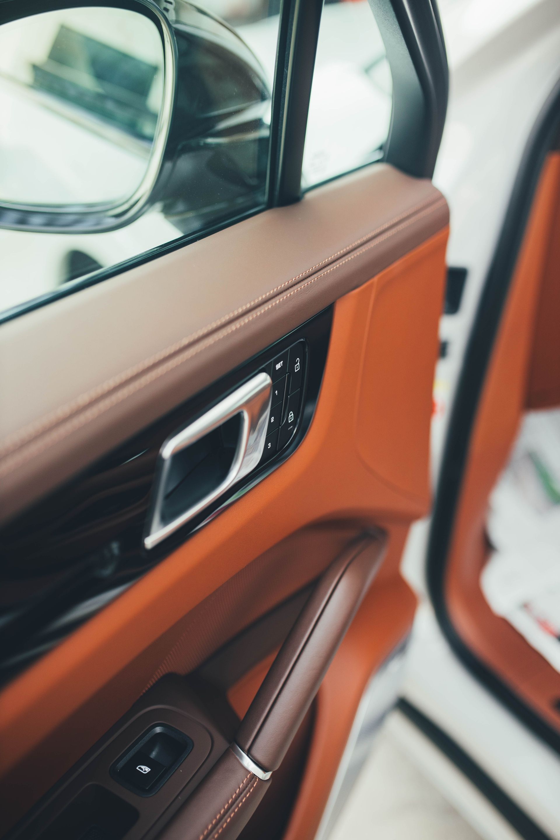 Car door interior with tan and orange trim, silver handle, and window mirror visible