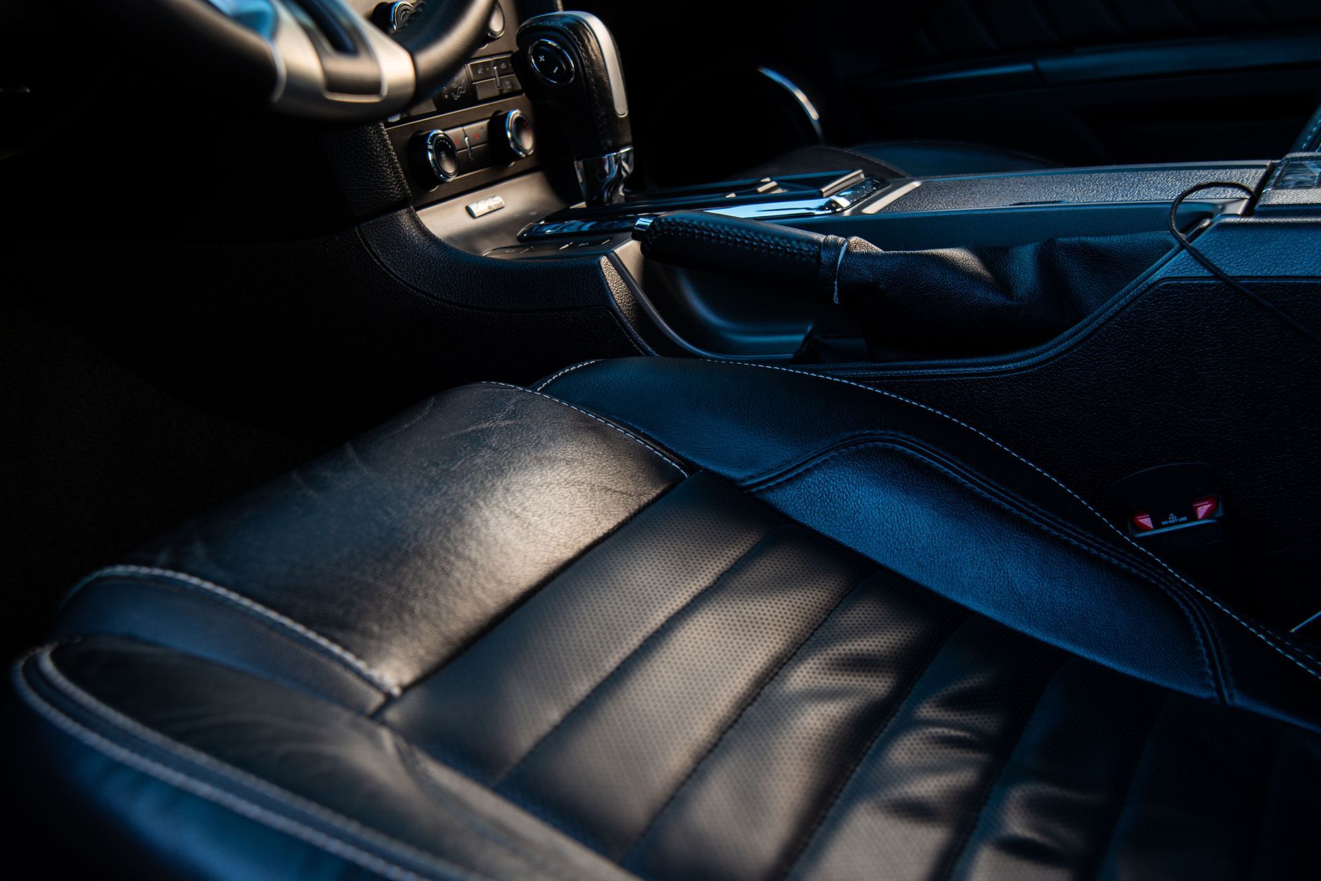 Black leather car seats and center console in a dimly lit interior, with blue highlights.