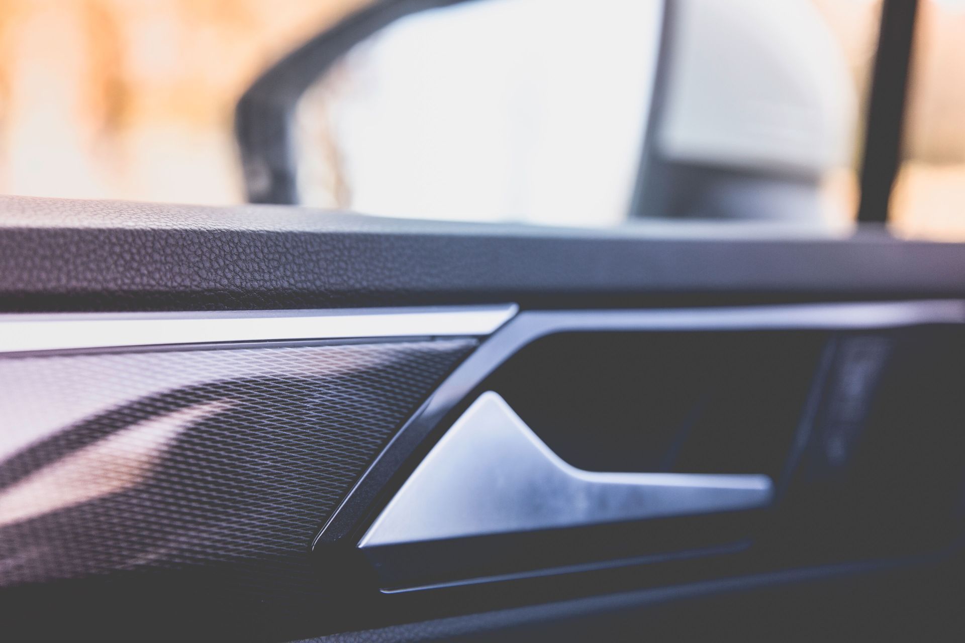 Close-up of a black car door interior with silver trim and a blurred seat in the background
