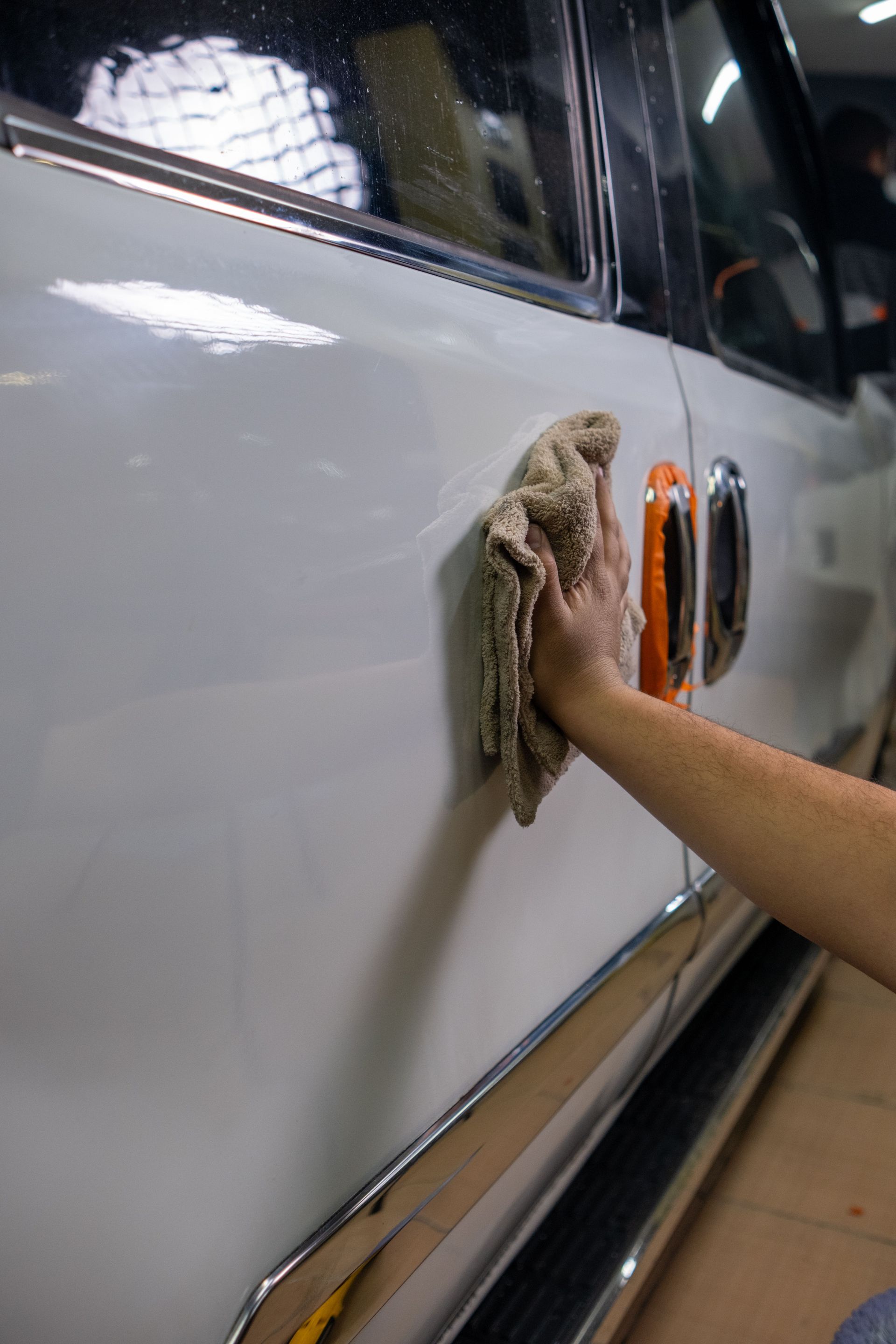 Person wiping a white car door with a cloth in a garage or car wash setting