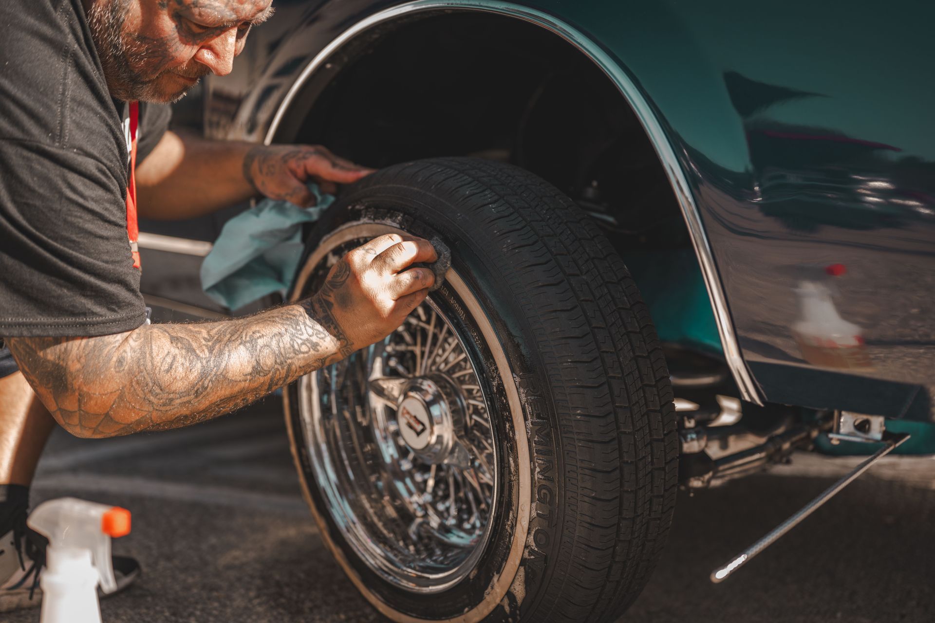 Detailing a car wheel and tire with a polishing brush near a dark green vehicle