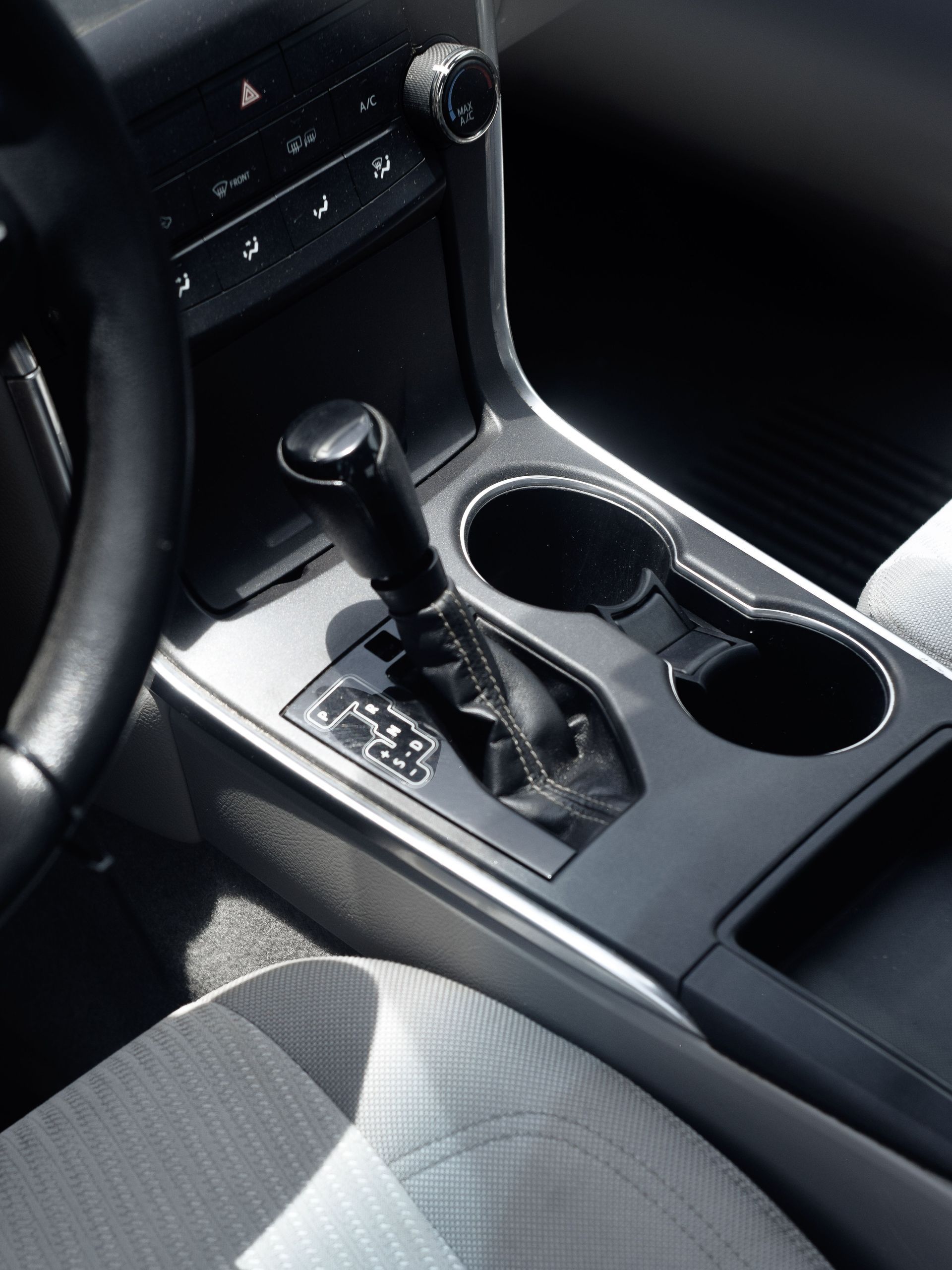 Car interior center console with automatic gear shifter and two cup holders, black trim and gray seats