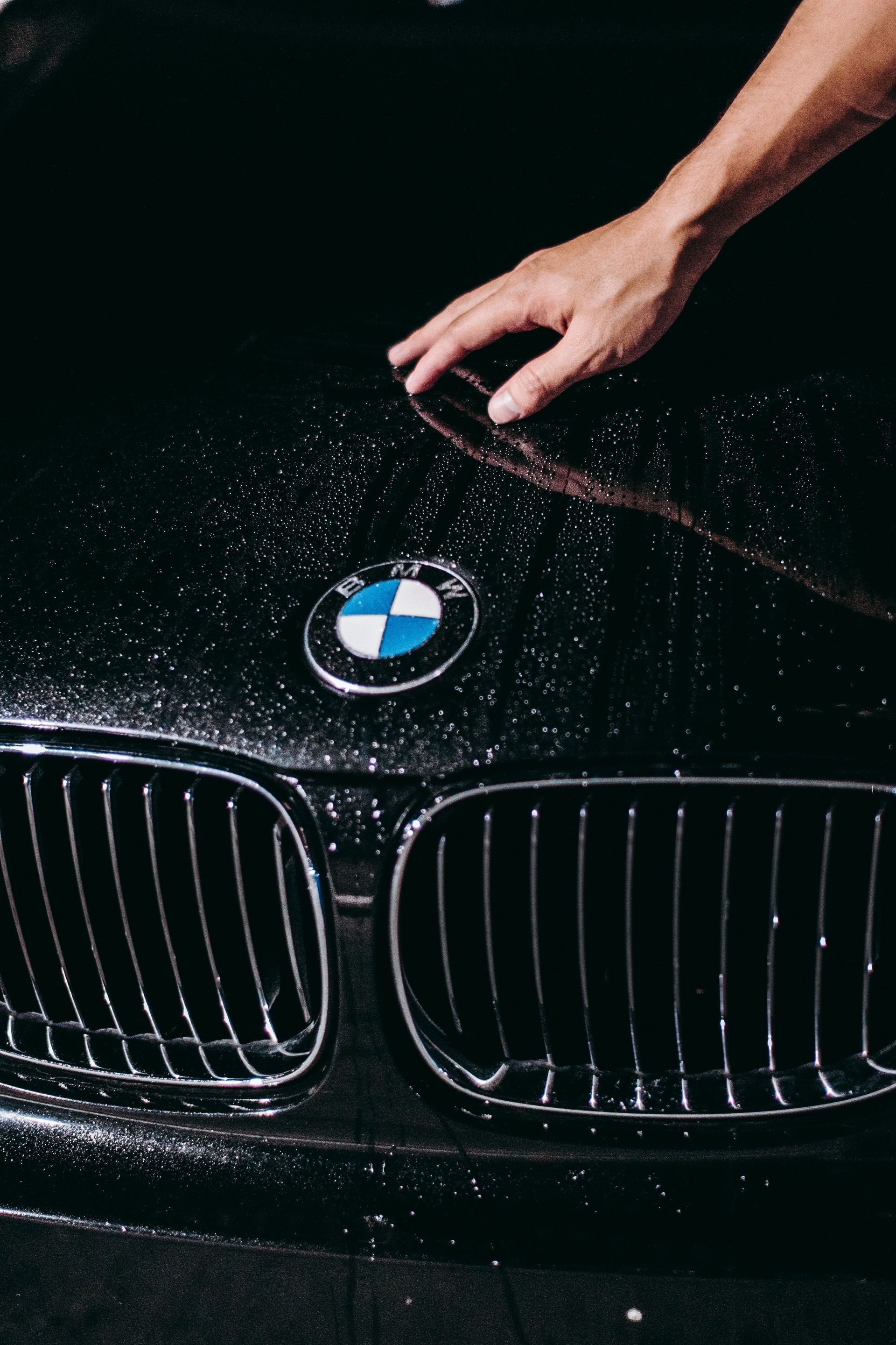 Hand wiping water off a black BMW hood with the grille and logo visible