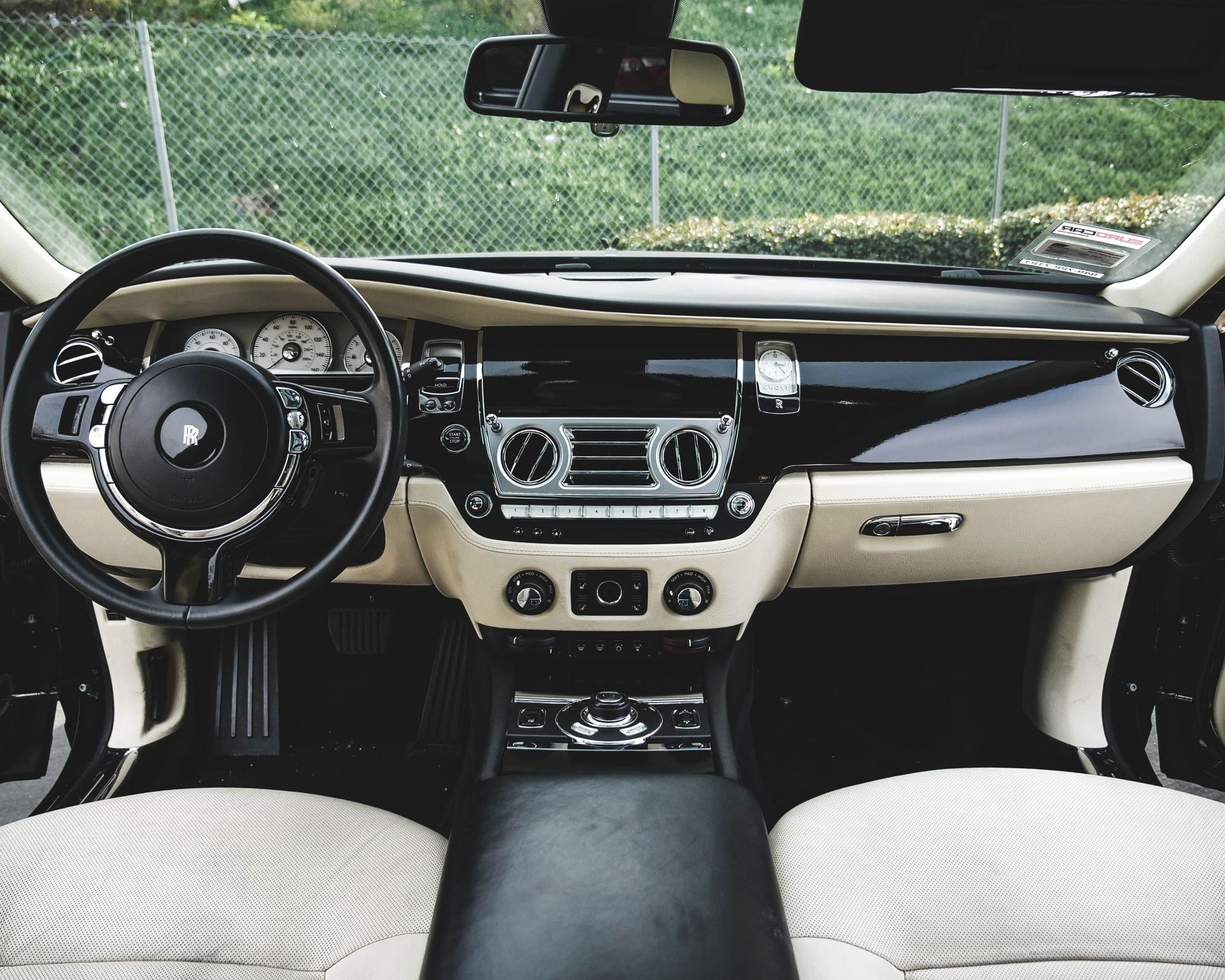 Classic car interior with black-and-white dashboard and steering wheel, viewed from the back seat.