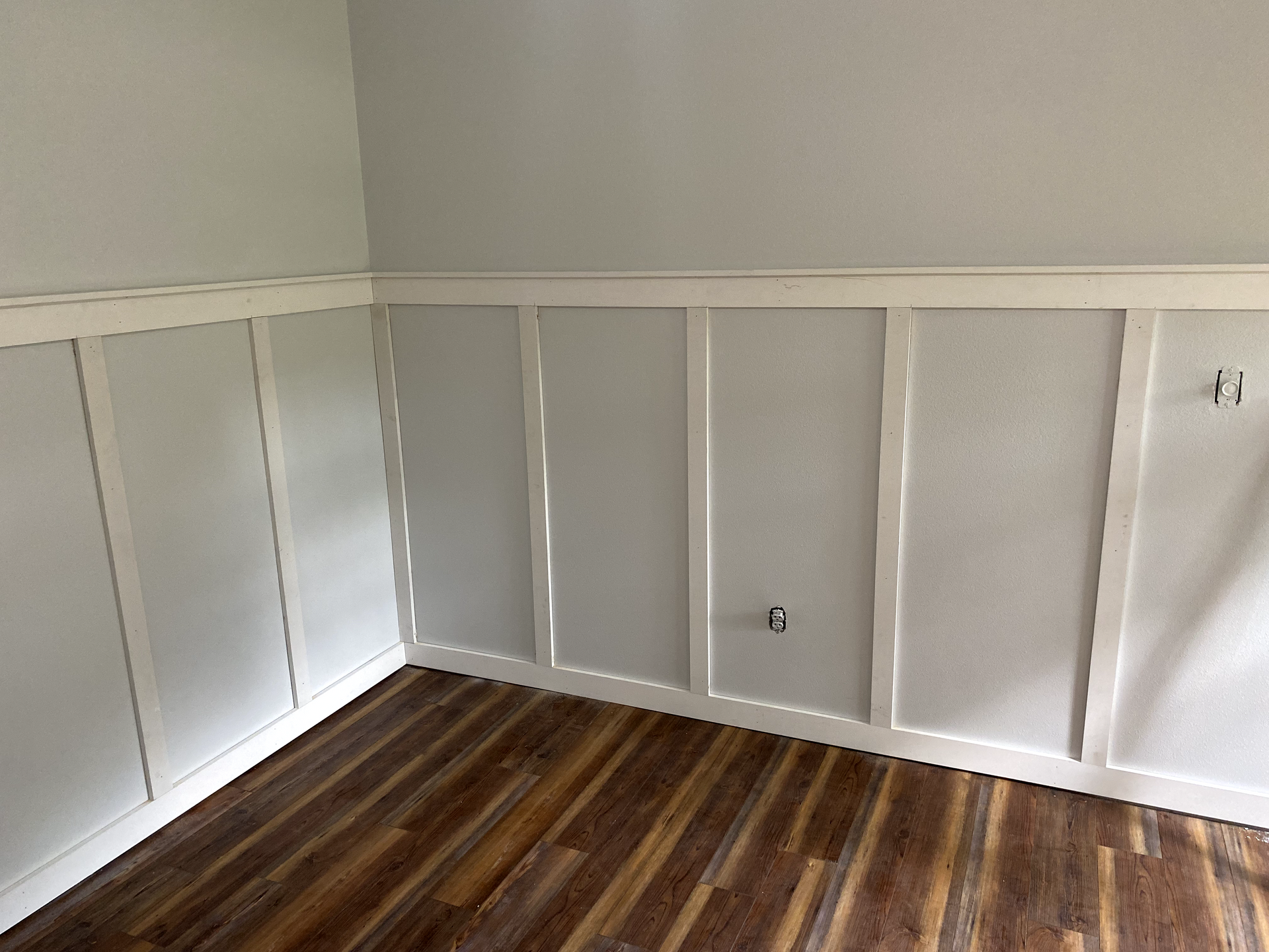 Room with gray wainscoting and light gray walls, wooden floor.