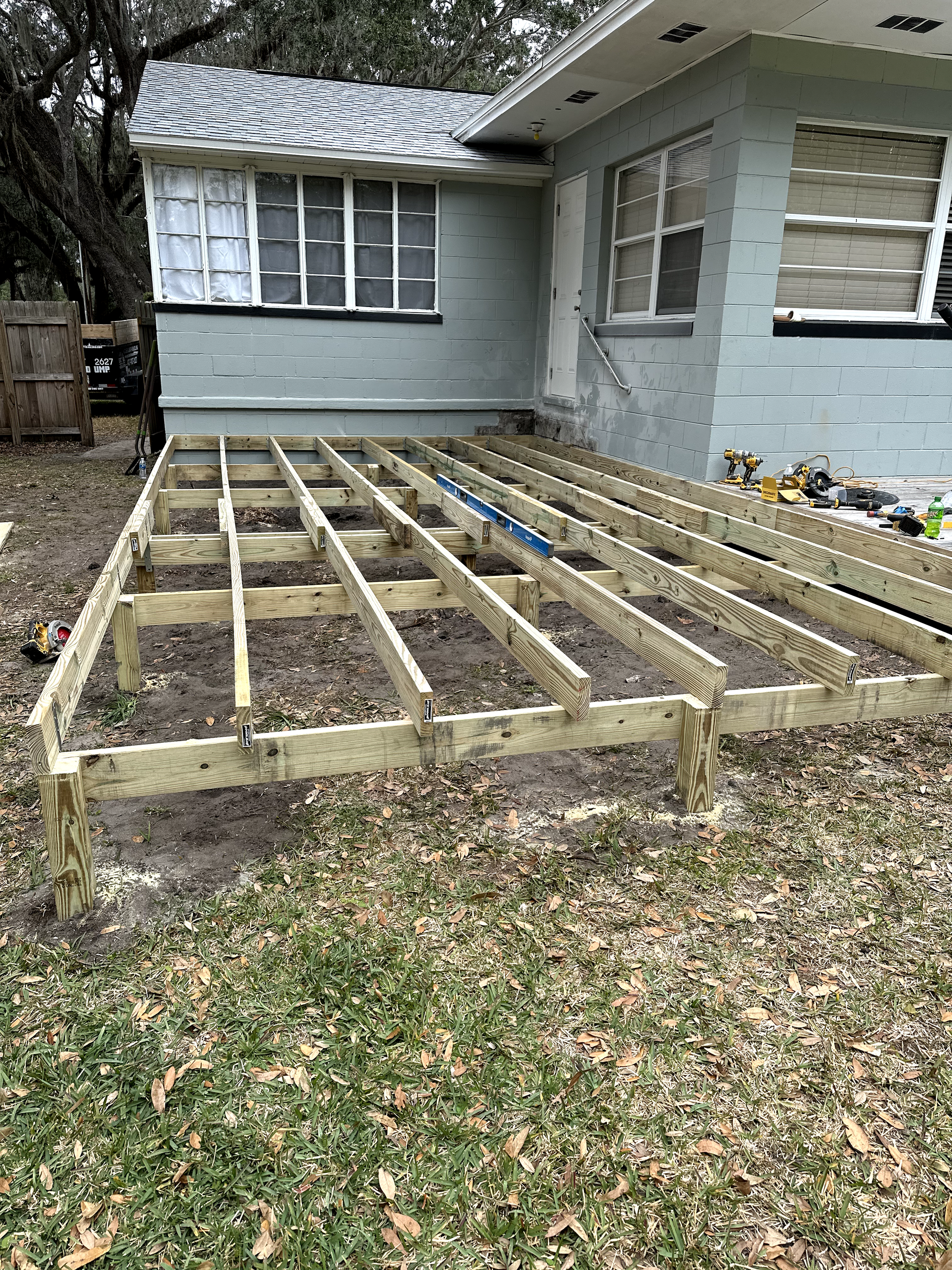 Newly built wooden deck frame next to a light blue house, set on a grassy yard.