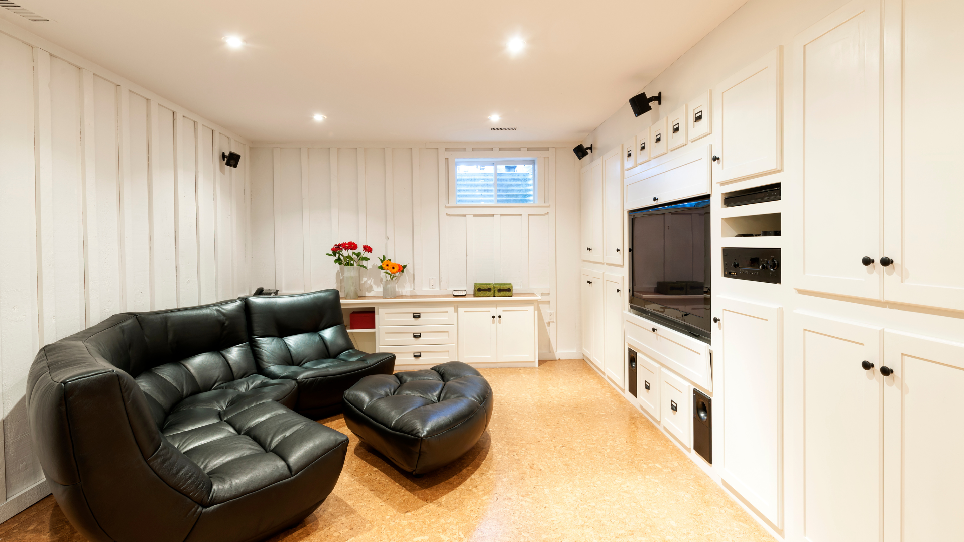 Black leather sofa in a white-walled entertainment room with a built-in TV and cabinets.