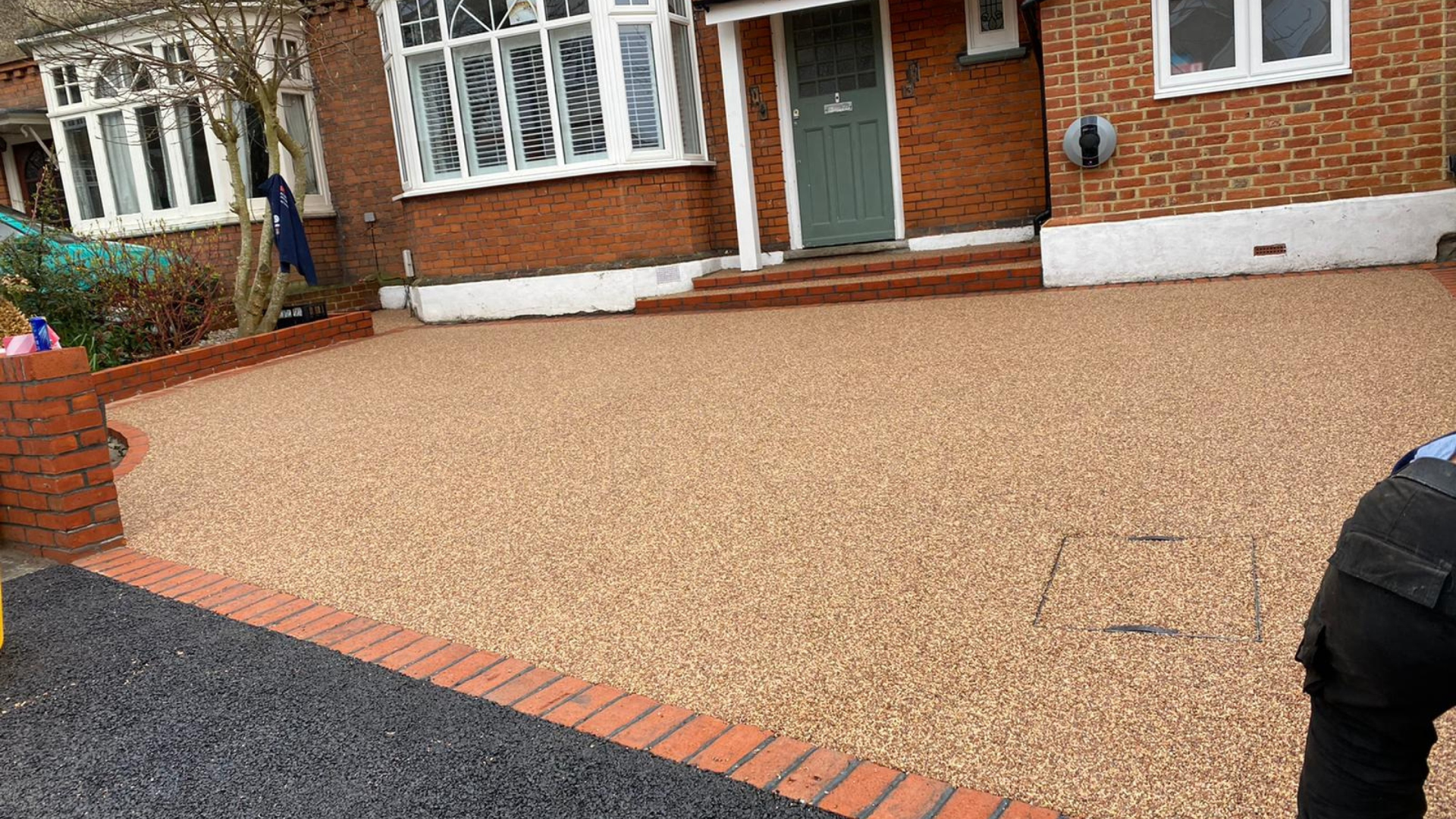 Tan gravel driveway in front of a brick house with a person on the right.