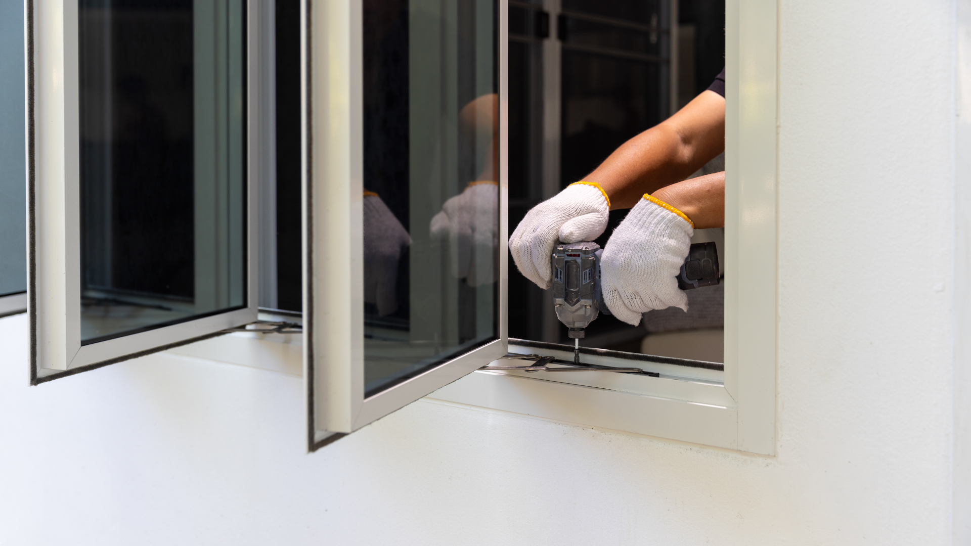 Person in work gloves using a drill to install a window.