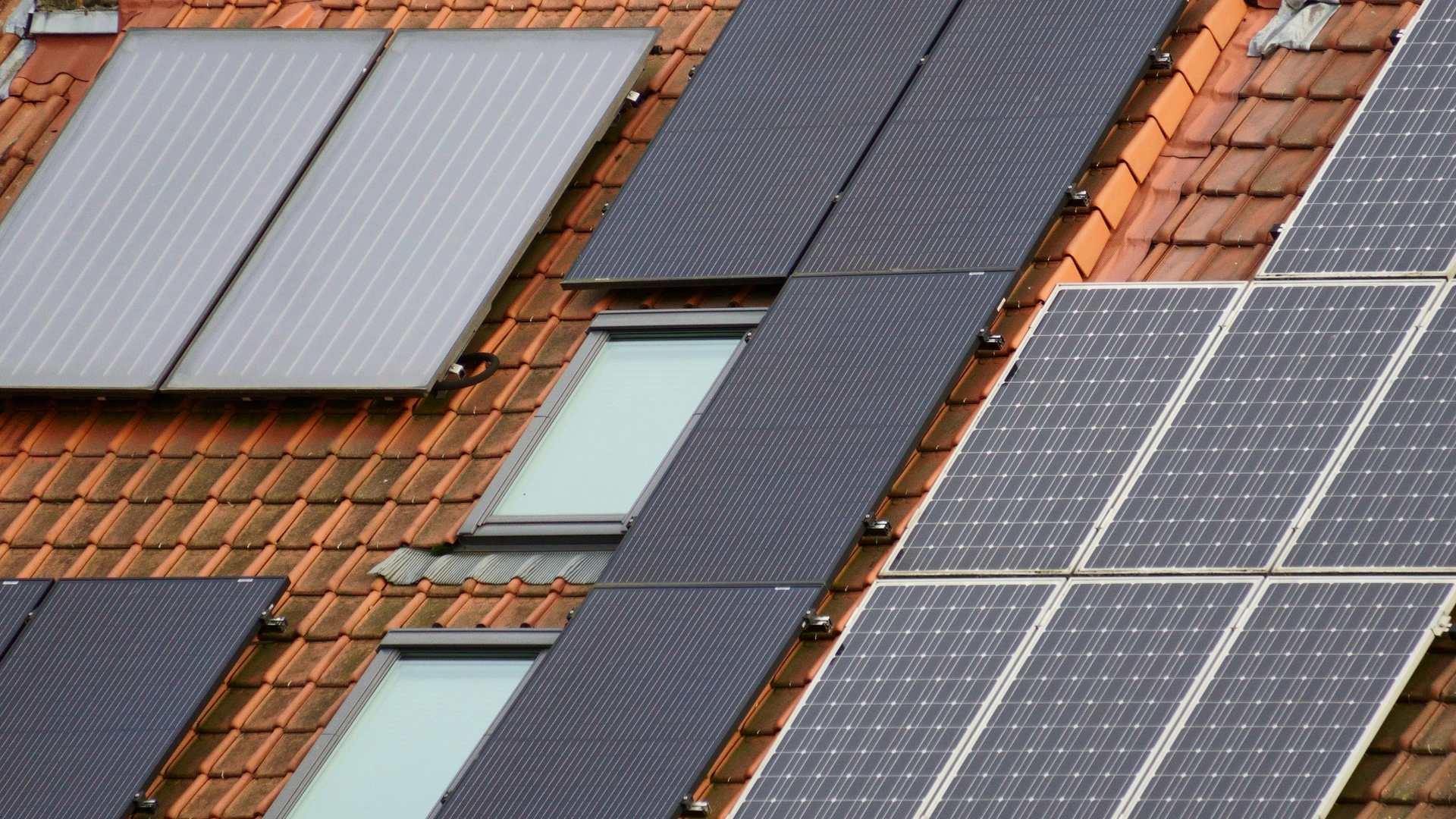Solar panels on a red tile roof with two windows.