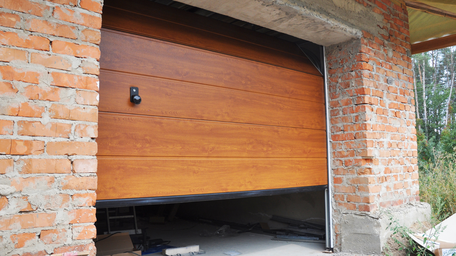 Brown garage door partially open in a brick building.