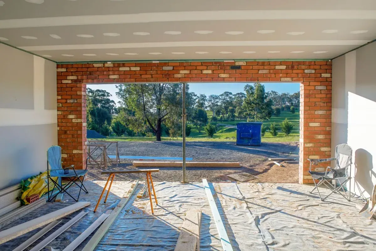 Interior view of a building under construction, showing a brick opening looking out onto a rural landscape.