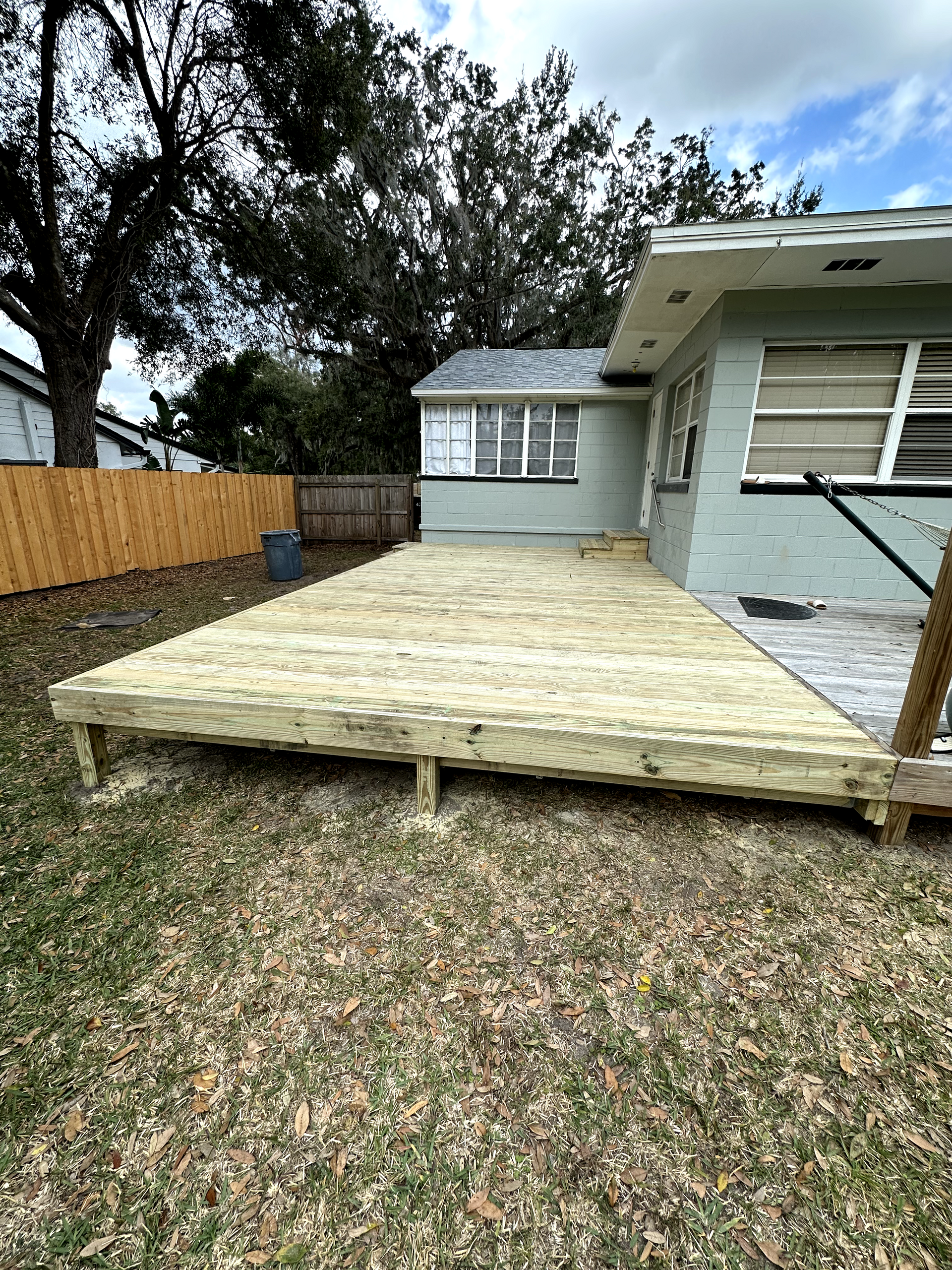 Wooden deck attached to a light-colored house. Deck overlooks patchy green lawn.