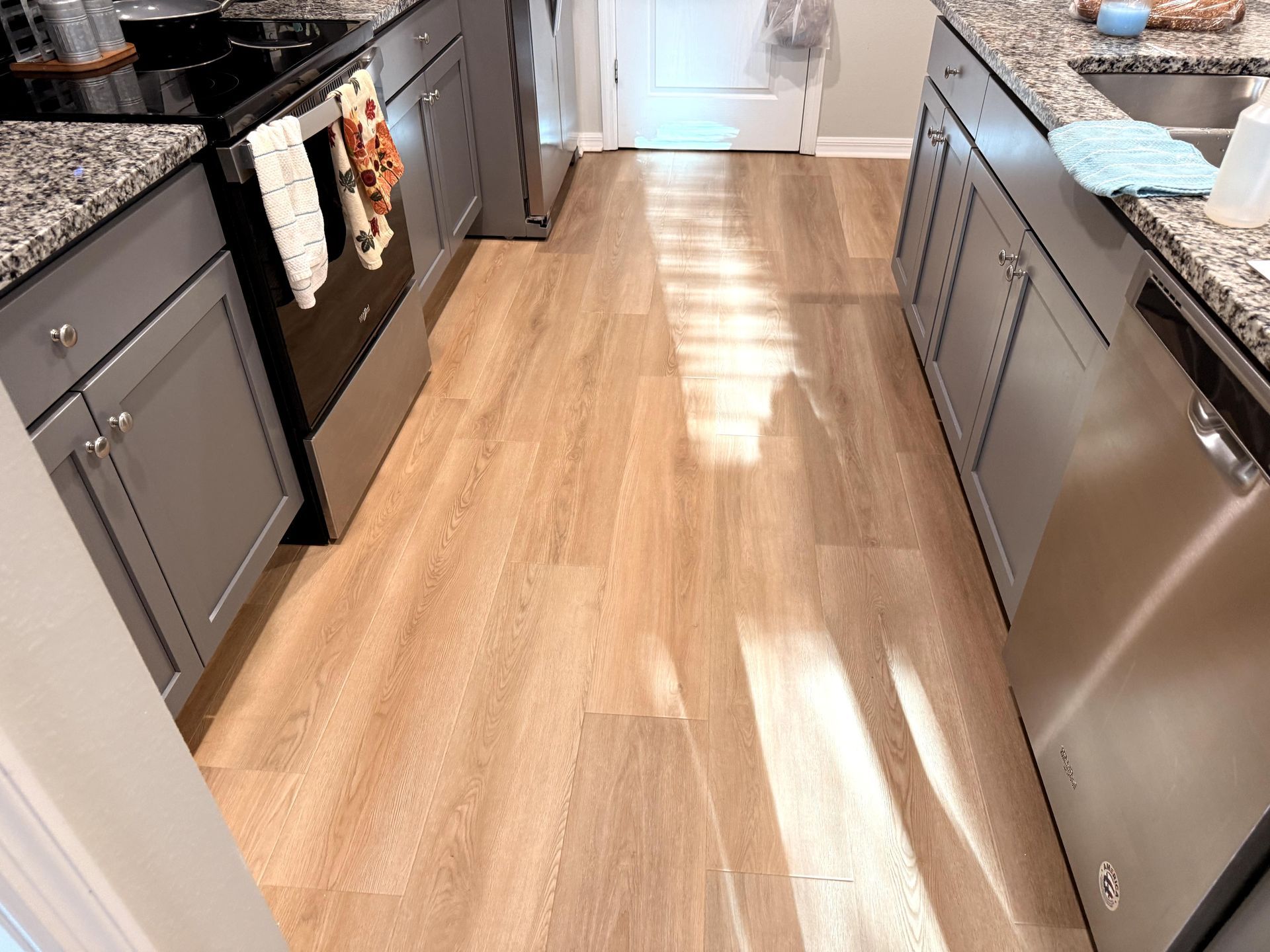 Kitchen with light wood-look flooring, gray cabinets, stainless steel appliances, and granite countertops.