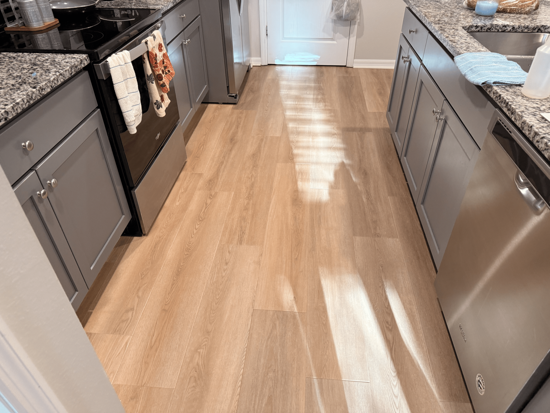 Kitchen with light wood-look flooring, stainless steel appliances, and gray cabinets. 