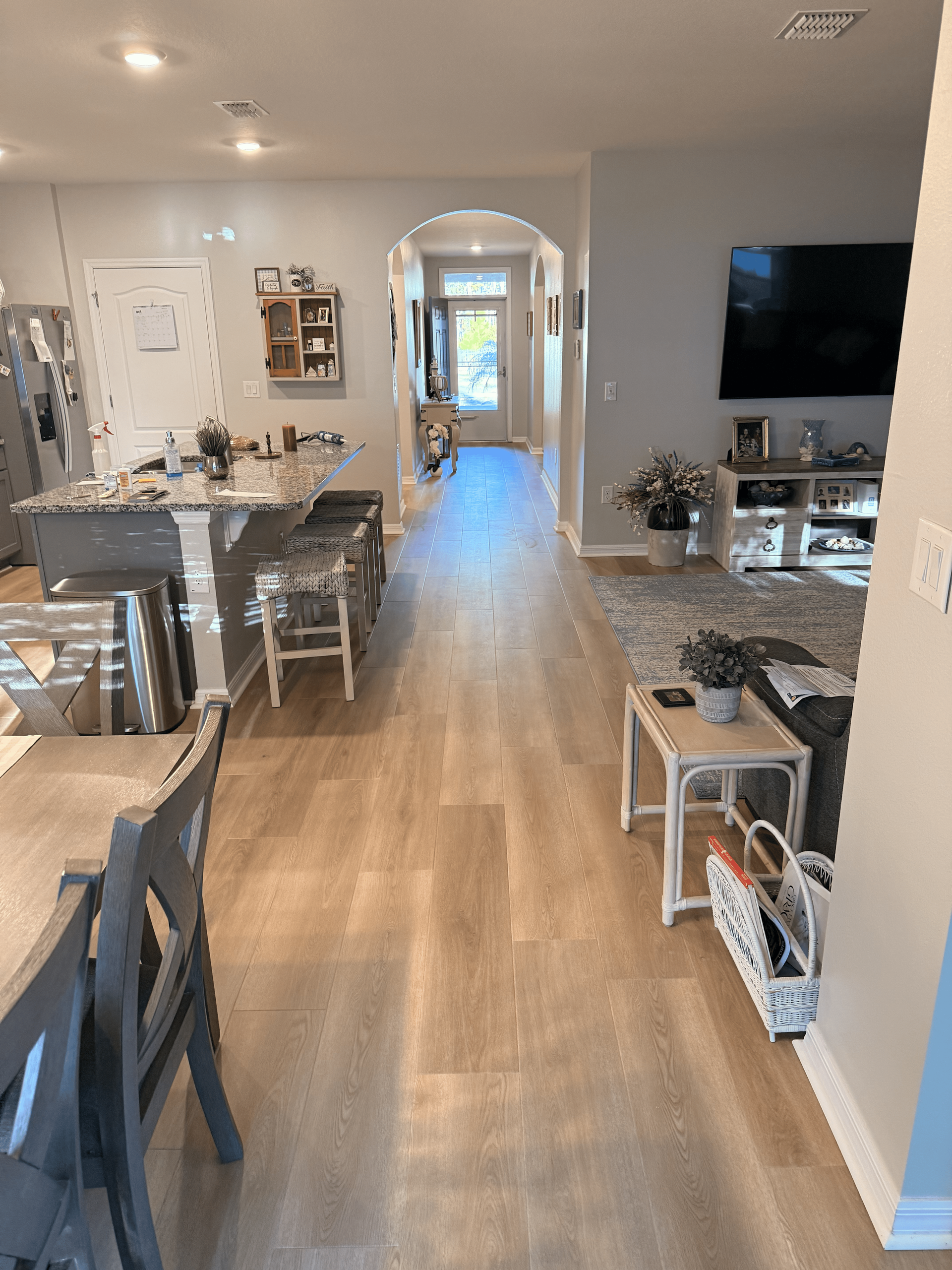 Interior view of a home with light wood flooring. Kitchen, living room, and hallway visible.