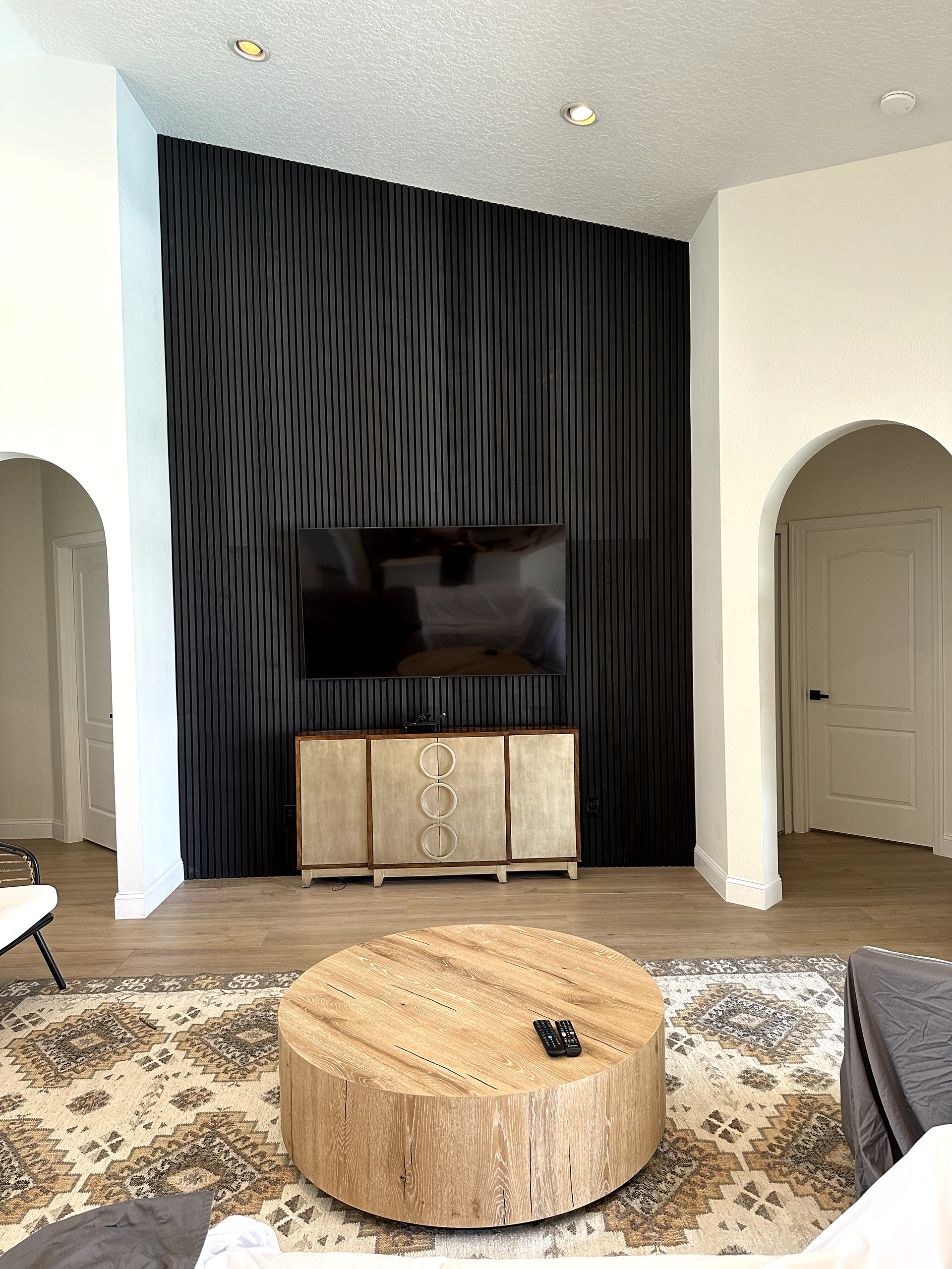 Living room with black paneled wall, TV, wooden cabinet, round coffee table, and patterned rug.