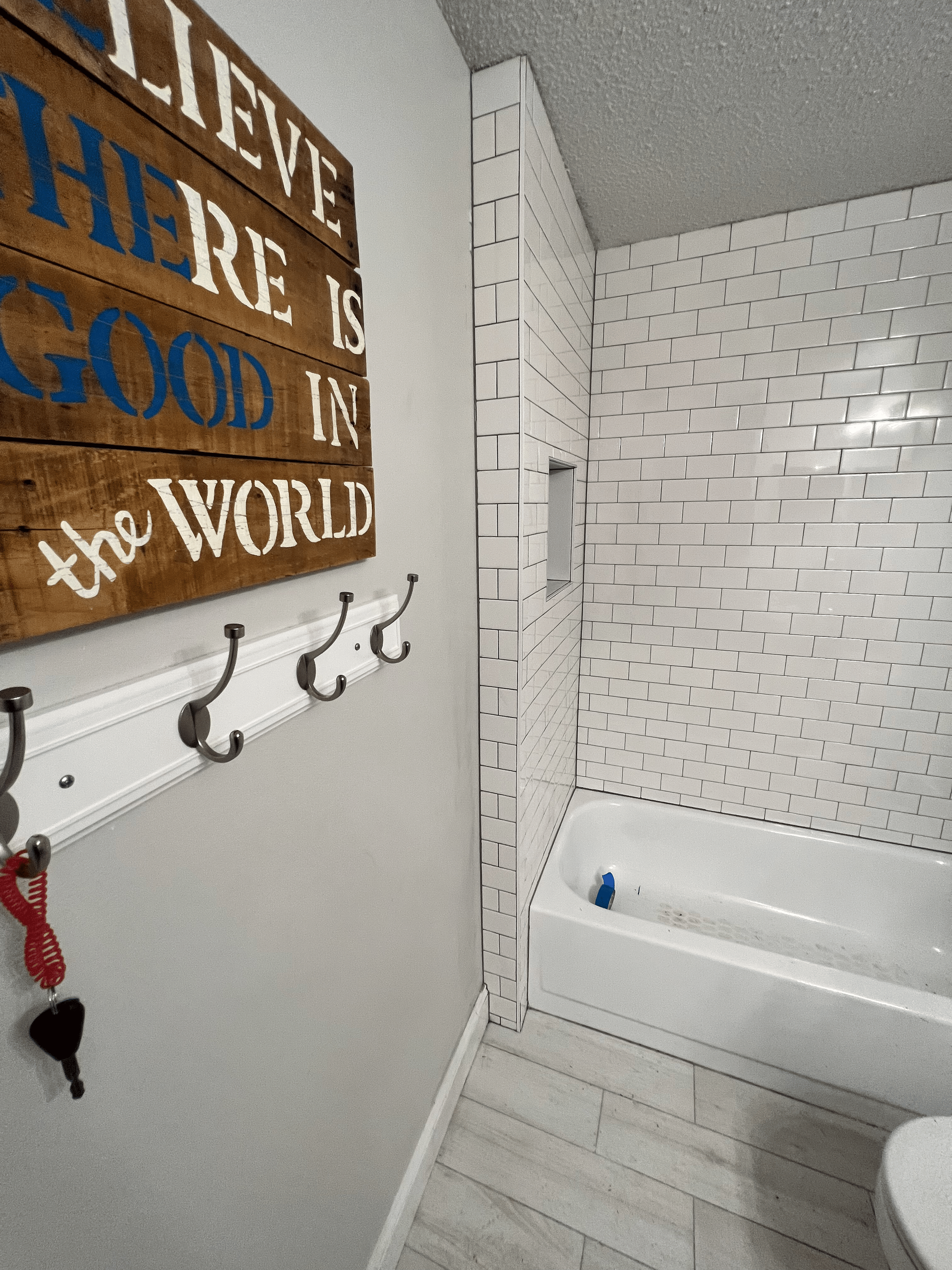 Bathroom with white subway tile shower, white tub, wooden sign, and coat rack.