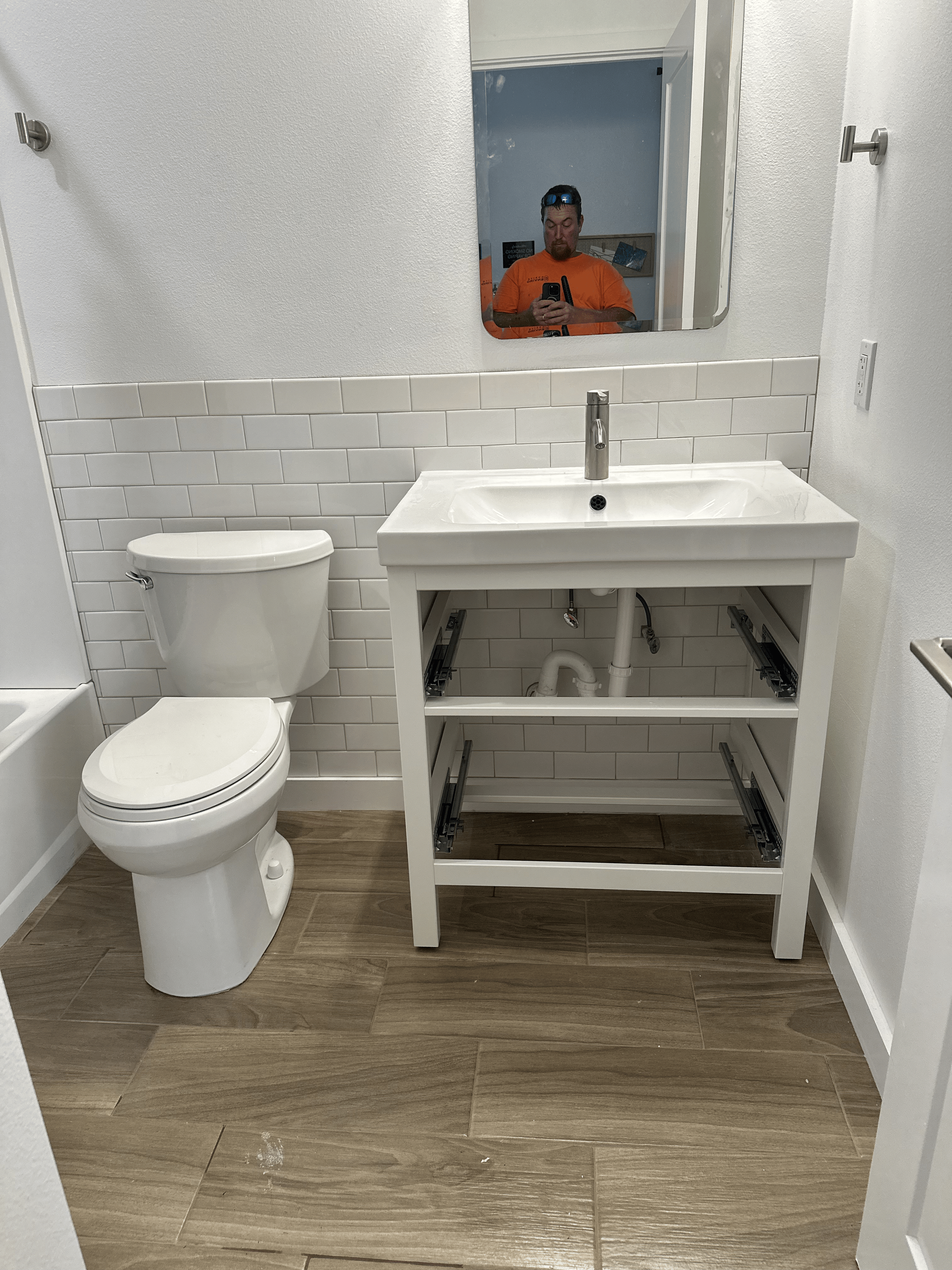 Bathroom renovation with white brick tile, a white sink, toilet, and light wood-look flooring. 