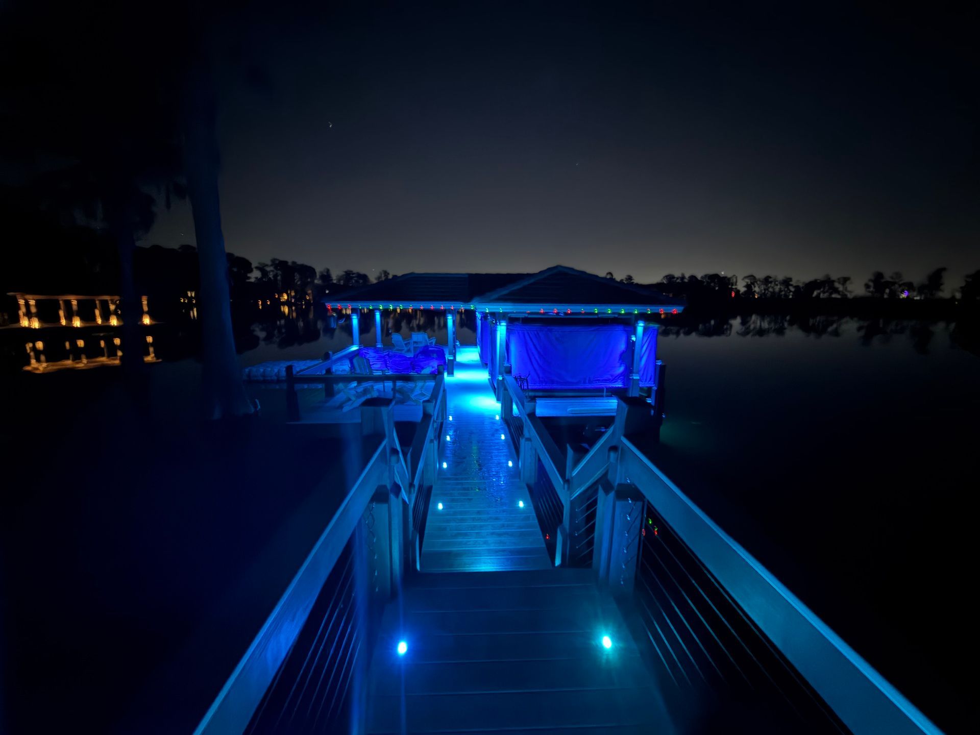 Night shot of a dock and boathouse illuminated with blue lights over dark water.